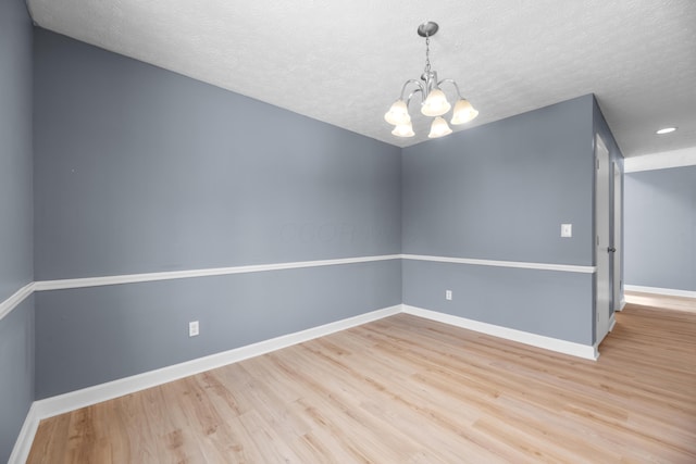 spare room featuring an inviting chandelier, wood finished floors, baseboards, and a textured ceiling