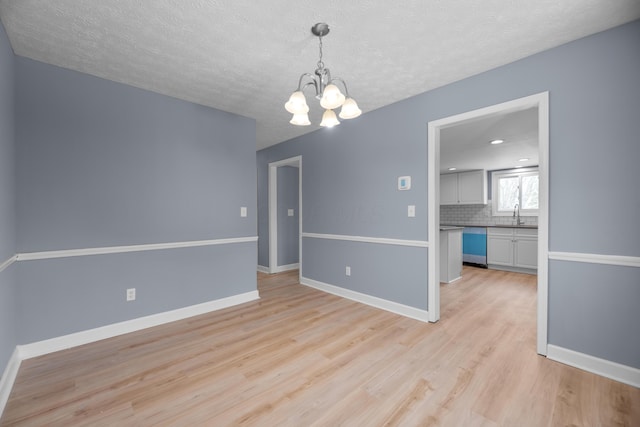 empty room featuring baseboards, light wood finished floors, a sink, a textured ceiling, and a notable chandelier