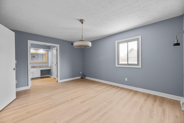 spare room with light wood-style floors, baseboards, and a textured ceiling