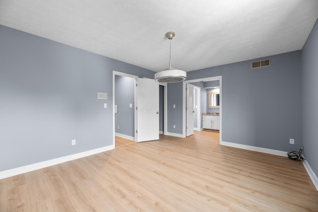 empty room featuring visible vents, baseboards, a textured ceiling, and light wood-style flooring