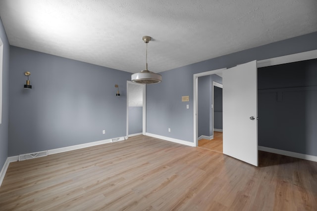 spare room with baseboards, visible vents, a textured ceiling, and light wood-style floors