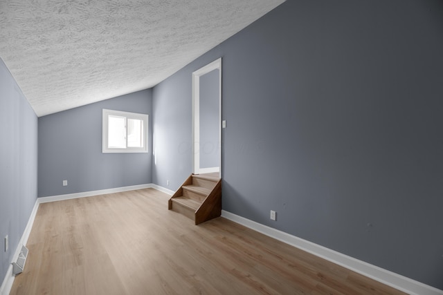 additional living space featuring visible vents, baseboards, vaulted ceiling, light wood-style floors, and a textured ceiling