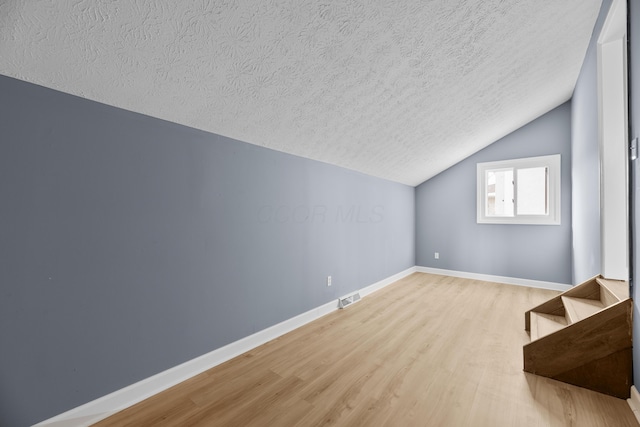 bonus room featuring stairway, wood finished floors, visible vents, baseboards, and a textured ceiling