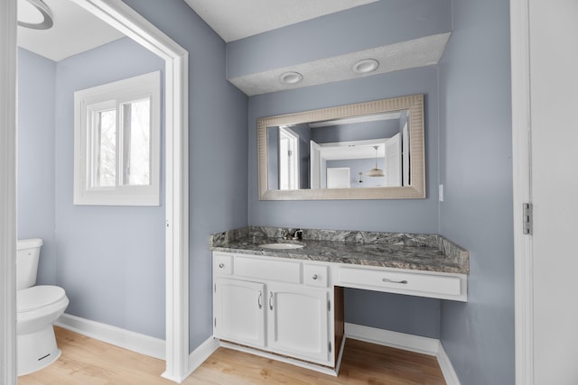 half bath with baseboards, toilet, wood finished floors, and vanity