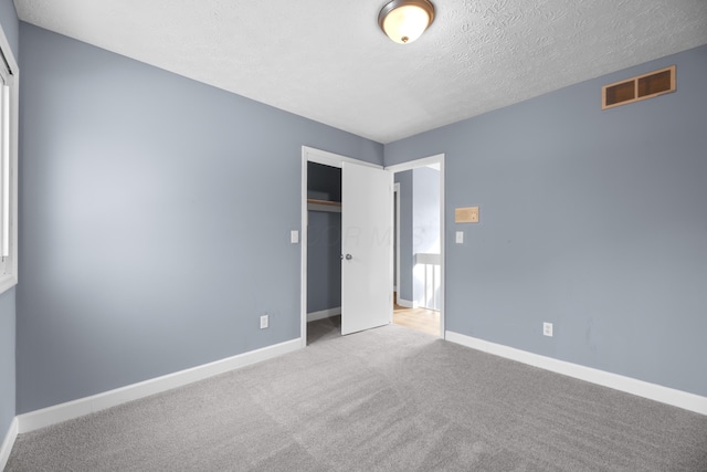 unfurnished bedroom featuring visible vents, a textured ceiling, a closet, carpet floors, and baseboards