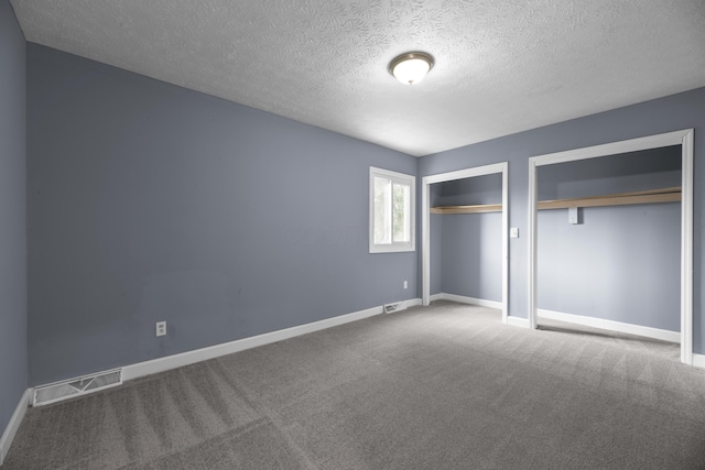 unfurnished bedroom featuring baseboards, visible vents, two closets, and carpet