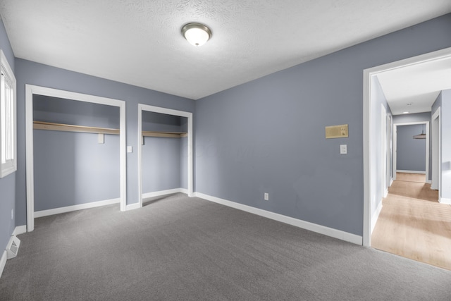 unfurnished bedroom featuring a textured ceiling, carpet, multiple closets, and baseboards