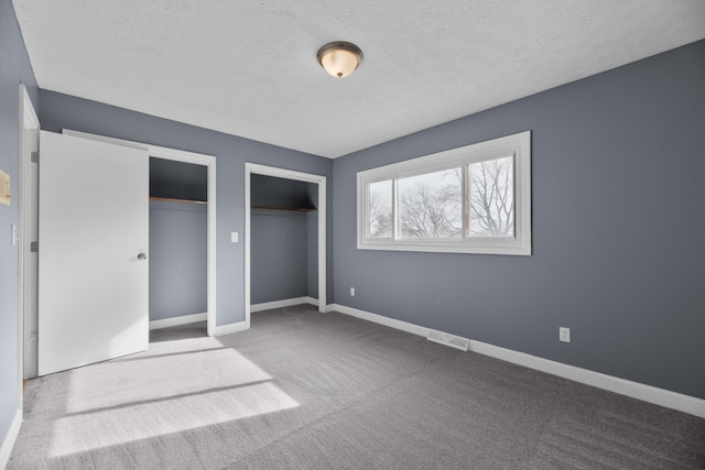 unfurnished bedroom featuring carpet, baseboards, visible vents, multiple closets, and a textured ceiling