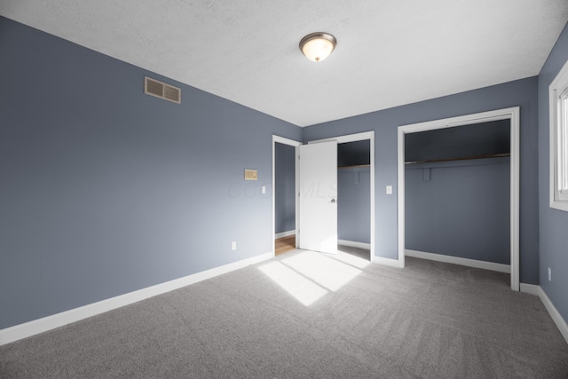 unfurnished bedroom featuring carpet, visible vents, baseboards, multiple closets, and a textured ceiling