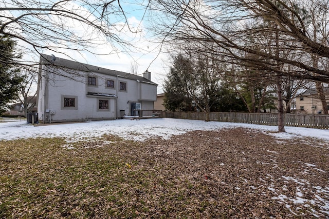 snow covered rear of property featuring central air condition unit, fence, a chimney, and stucco siding