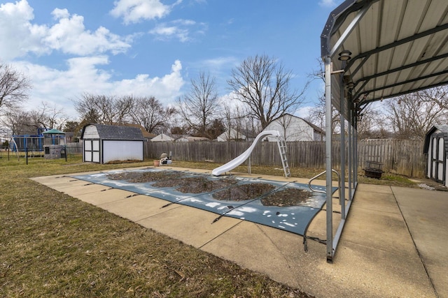 view of pool featuring a patio, a fenced backyard, an outbuilding, a storage unit, and a water slide