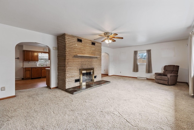 unfurnished living room with arched walkways, baseboards, a ceiling fan, carpet flooring, and a brick fireplace