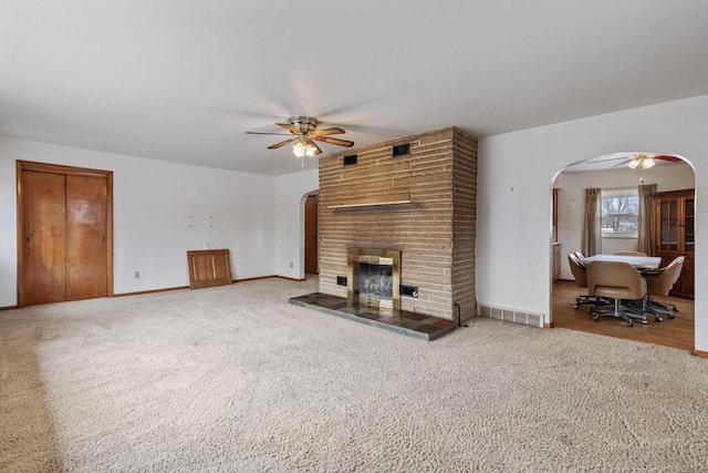 unfurnished living room featuring visible vents, arched walkways, ceiling fan, carpet floors, and a brick fireplace