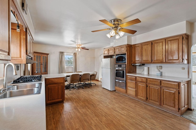 kitchen featuring brown cabinetry, oven, freestanding refrigerator, a sink, and a warming drawer