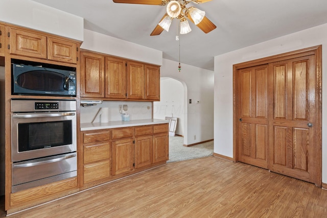 kitchen featuring arched walkways, brown cabinets, light wood-style floors, black microwave, and oven