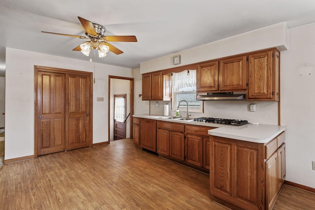 kitchen featuring brown cabinets, light countertops, light wood-style flooring, a sink, and under cabinet range hood