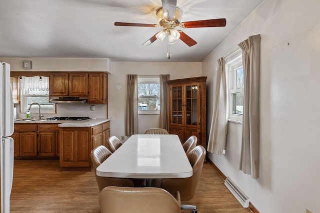 kitchen featuring light countertops, brown cabinets, under cabinet range hood, and wood finished floors