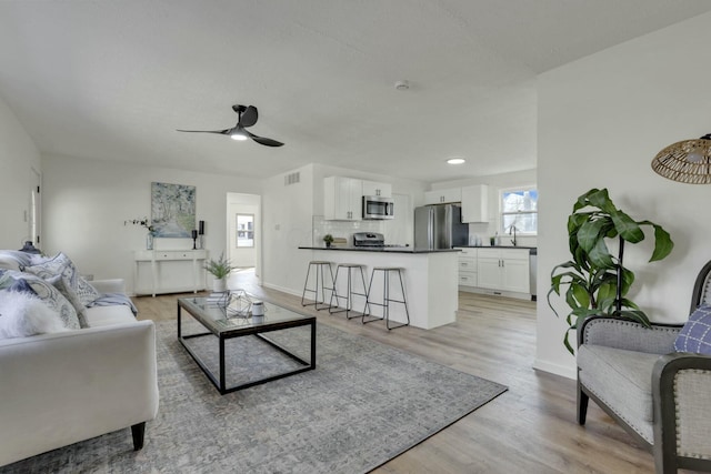 living room with baseboards, visible vents, a ceiling fan, and light wood-style floors