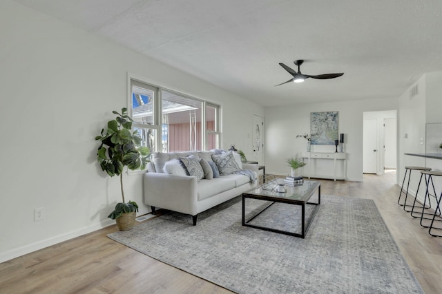 living room featuring visible vents, baseboards, ceiling fan, a textured ceiling, and light wood-style floors