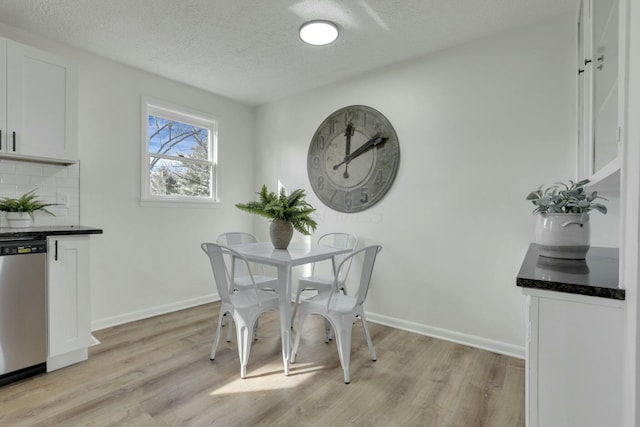 dining room featuring baseboards, a textured ceiling, and light wood finished floors