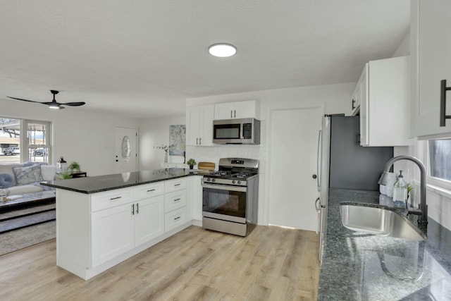 kitchen featuring stainless steel appliances, white cabinetry, a sink, dark stone counters, and a peninsula