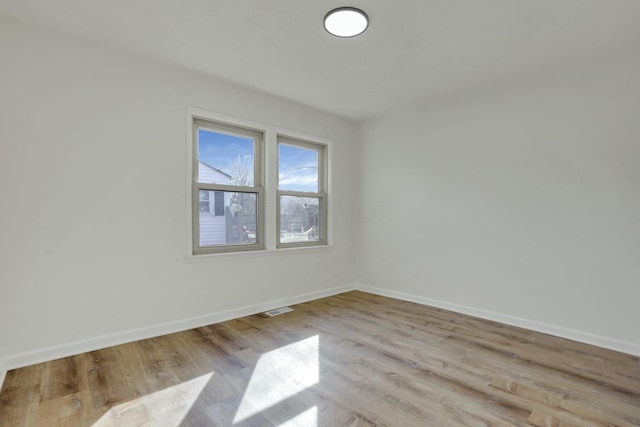 empty room with wood finished floors, visible vents, and baseboards