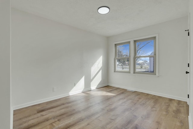 spare room featuring visible vents, a textured ceiling, baseboards, and wood finished floors