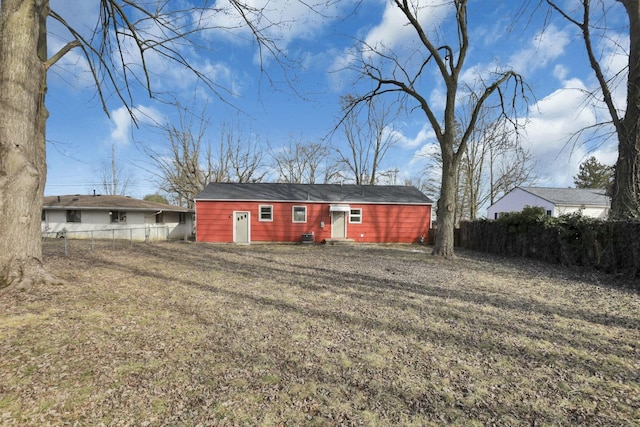 rear view of house with entry steps, a yard, and fence