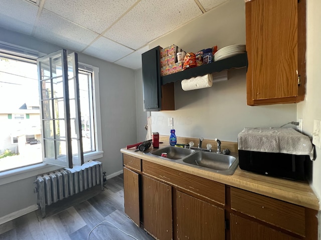 kitchen featuring radiator heating unit, wood finished floors, light countertops, a paneled ceiling, and a sink