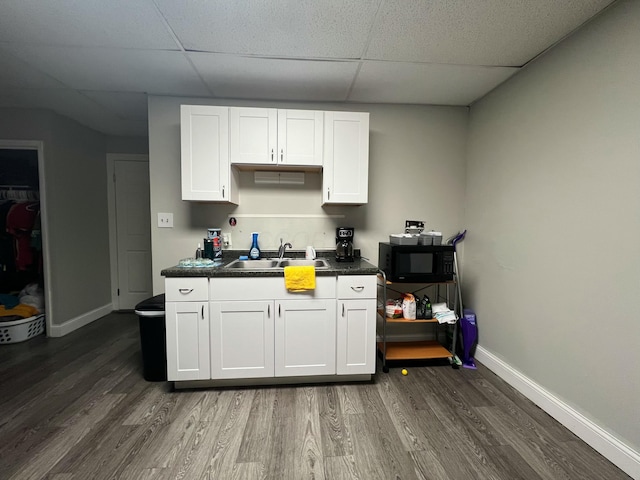 kitchen featuring black microwave, a sink, white cabinetry, dark countertops, and dark wood finished floors