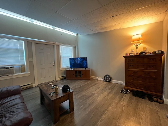 living room with cooling unit, a paneled ceiling, a baseboard heating unit, wood finished floors, and baseboards