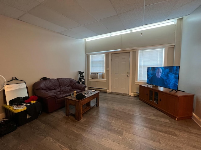 living area with a baseboard radiator, baseboard heating, wood finished floors, cooling unit, and a drop ceiling