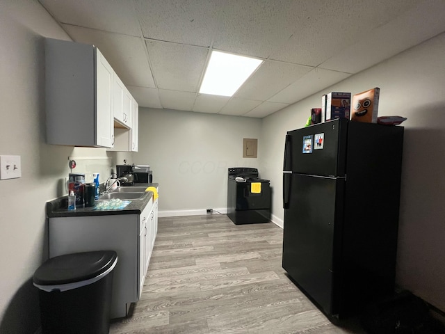 kitchen with dark countertops, light wood-type flooring, freestanding refrigerator, a paneled ceiling, and a sink