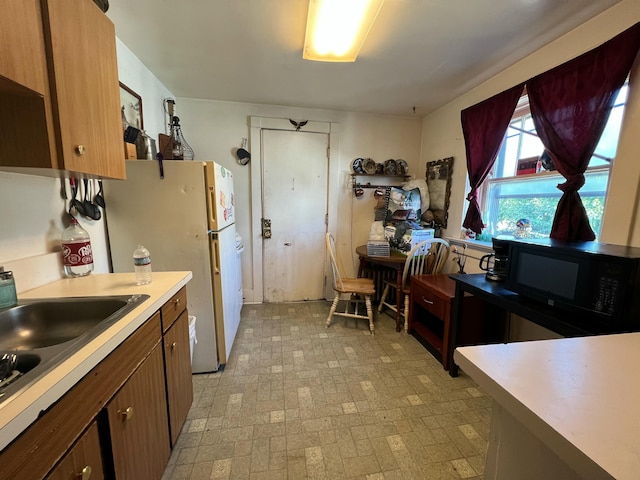 kitchen with brown cabinets, freestanding refrigerator, light countertops, black microwave, and a sink