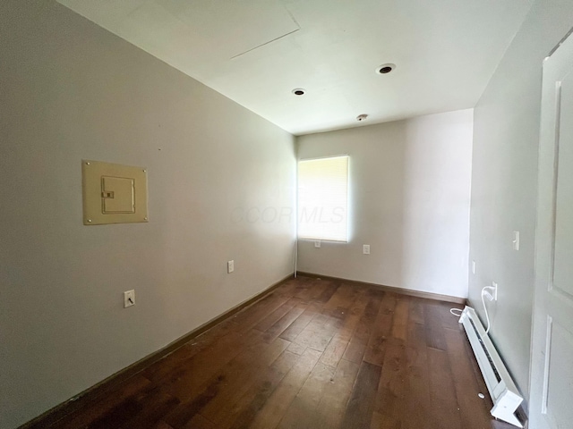 spare room featuring a baseboard heating unit, dark wood-type flooring, electric panel, and baseboards