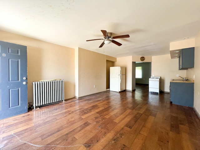 unfurnished living room with dark wood-style floors, radiator heating unit, a ceiling fan, a sink, and baseboards