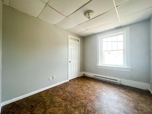 spare room with a baseboard heating unit, a paneled ceiling, stone finish floor, and baseboards