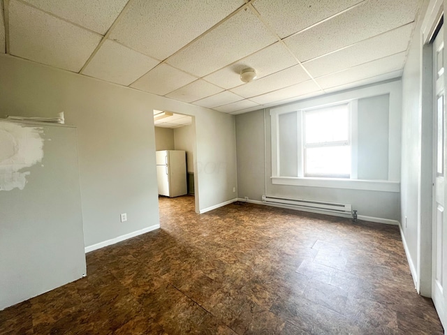 unfurnished room with a baseboard heating unit, a paneled ceiling, and baseboards