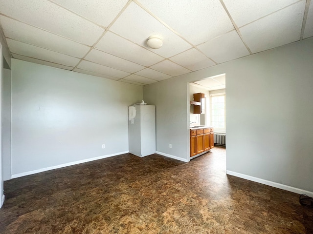 unfurnished room featuring baseboards, a drop ceiling, and radiator