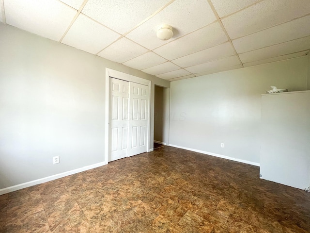 unfurnished bedroom featuring a closet, a drop ceiling, and baseboards