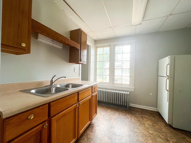 kitchen with a drop ceiling, a sink, freestanding refrigerator, and radiator