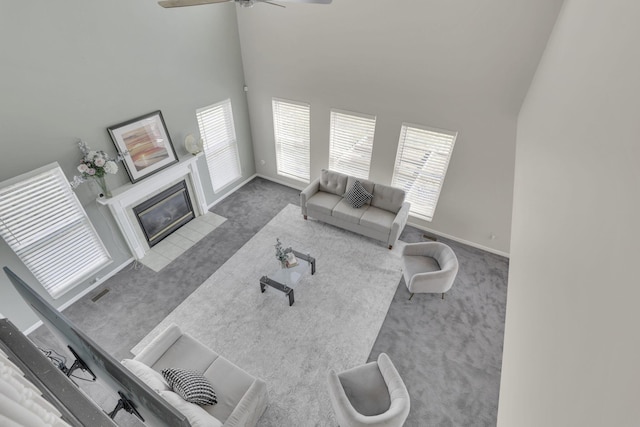 living room with a tiled fireplace, baseboards, a towering ceiling, and carpet floors