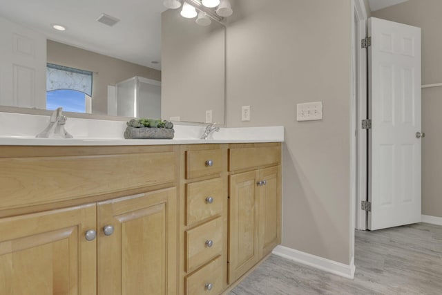 bathroom featuring wood finished floors, visible vents, baseboards, double vanity, and a sink