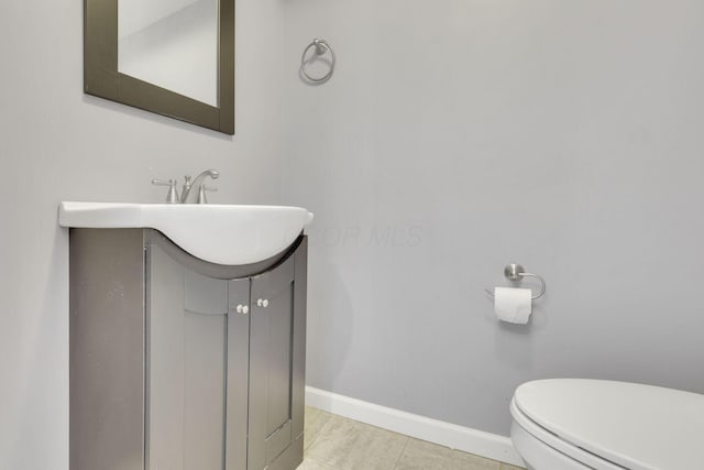 half bath with tile patterned floors, baseboards, toilet, and vanity