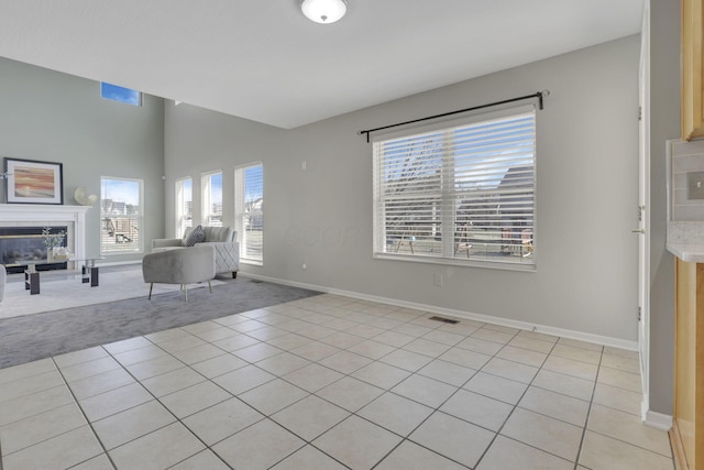 unfurnished living room featuring a tiled fireplace, light tile patterned floors, visible vents, and baseboards