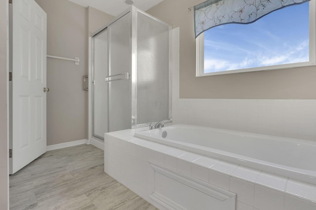 full bathroom featuring a shower stall, a garden tub, wood finished floors, and baseboards