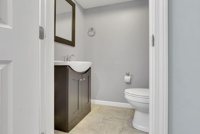 half bathroom with vanity, tile patterned floors, toilet, and baseboards