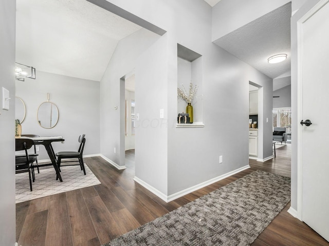 corridor featuring dark wood-style floors, lofted ceiling, a textured ceiling, and baseboards