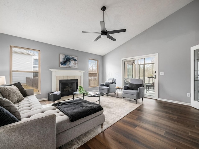 living room with a textured ceiling, dark wood-type flooring, a ceiling fan, baseboards, and a tiled fireplace