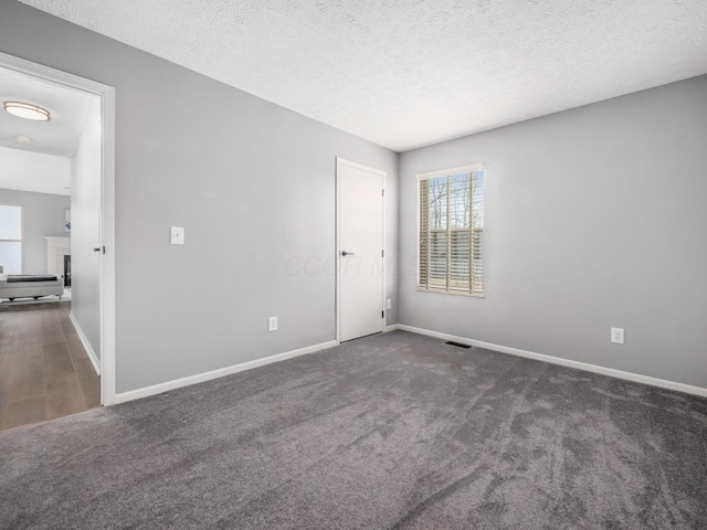 carpeted spare room with baseboards, a fireplace, visible vents, and a textured ceiling